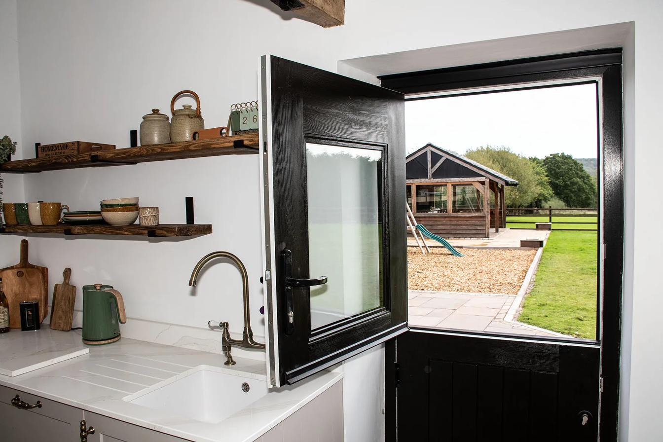 The Greens Farmhouse guest kitchenette with rustic wood shelving, farmhouse sink and doorway looking out to the garden